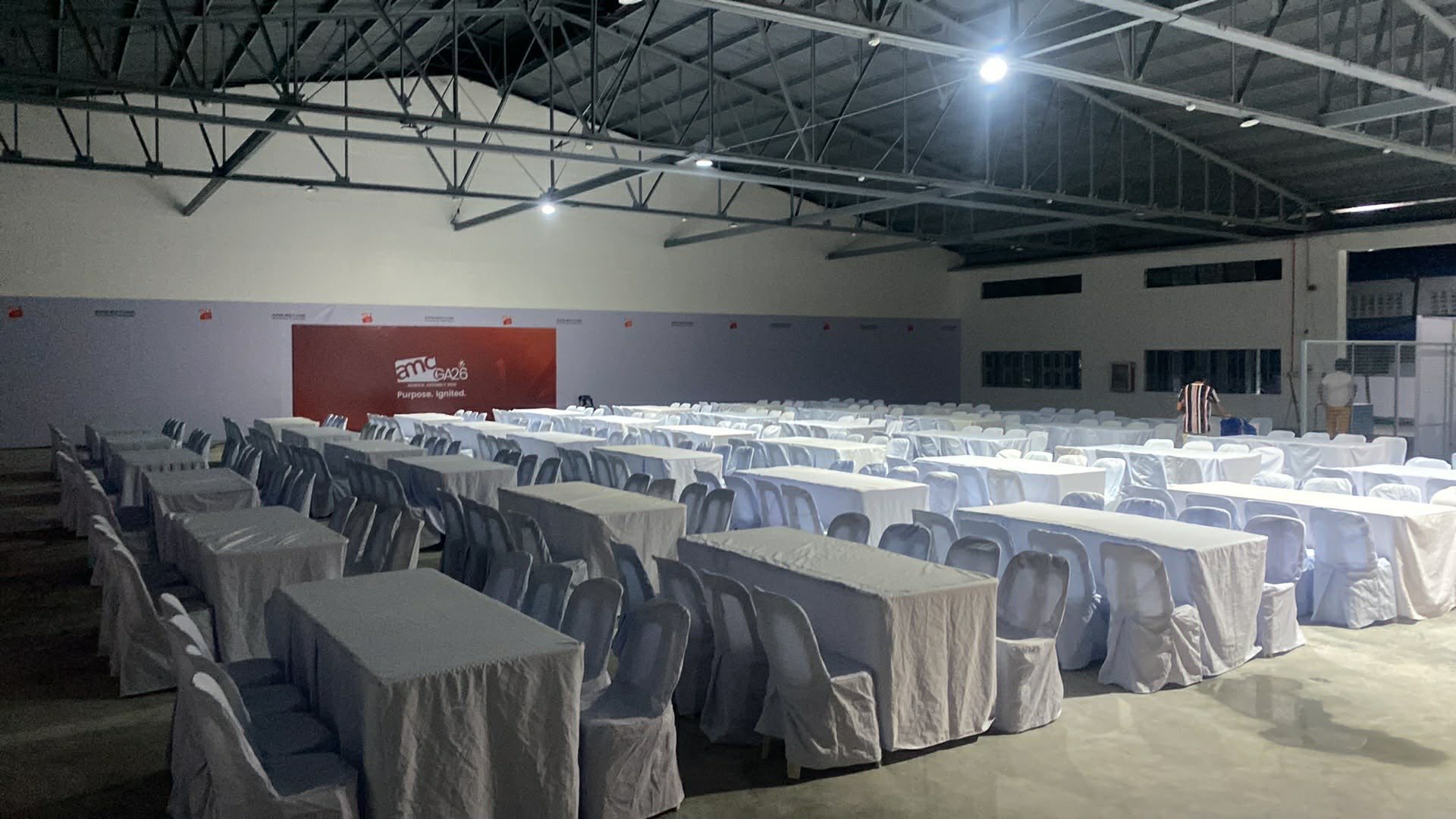 Rectangular tables and chairs dressed in white covers and skirting for a company program inside a covered venue
