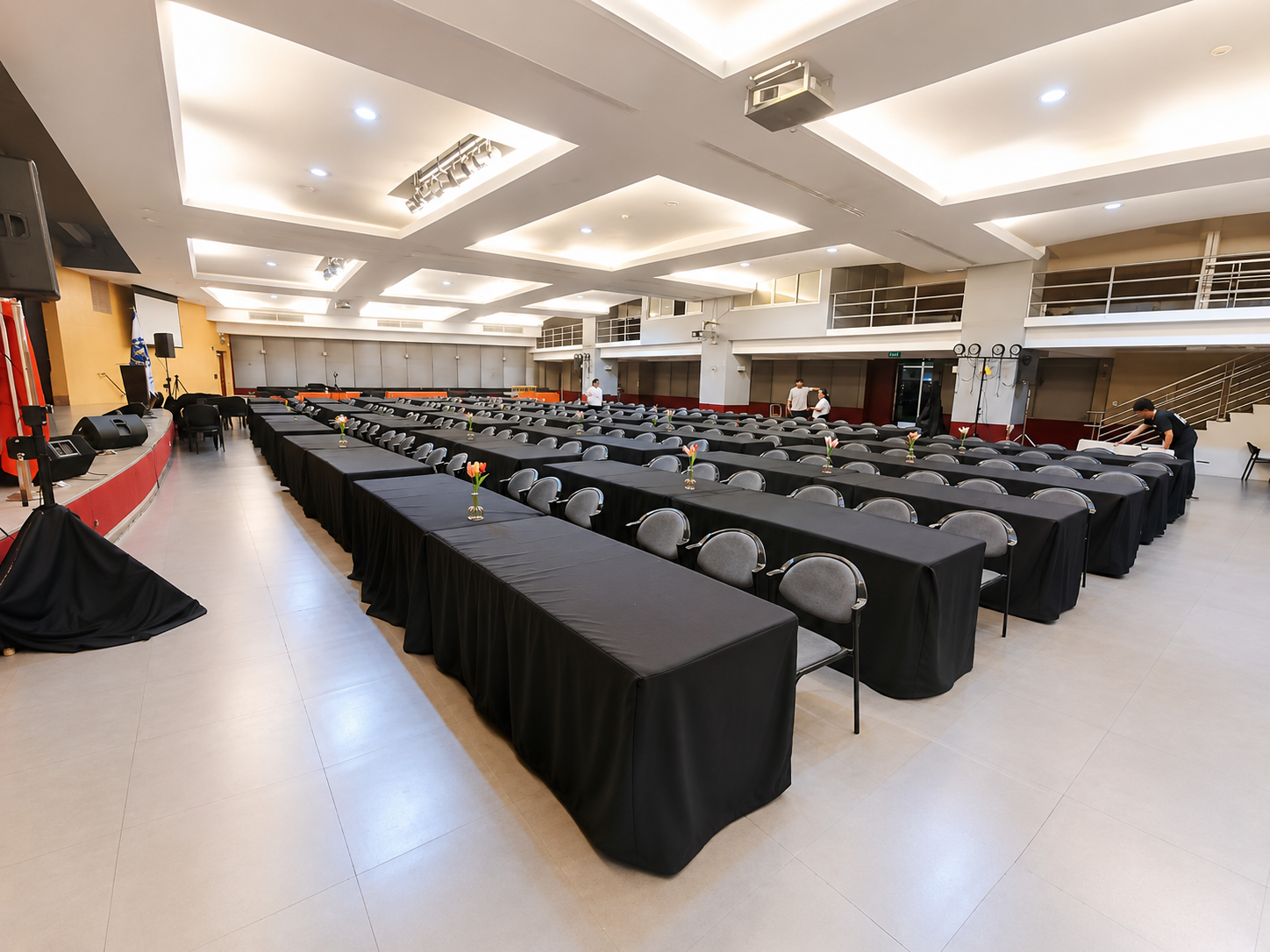 Long banquet tables in black linens with cushioned chairs and flower centerpieces set for a seminar in a function hall