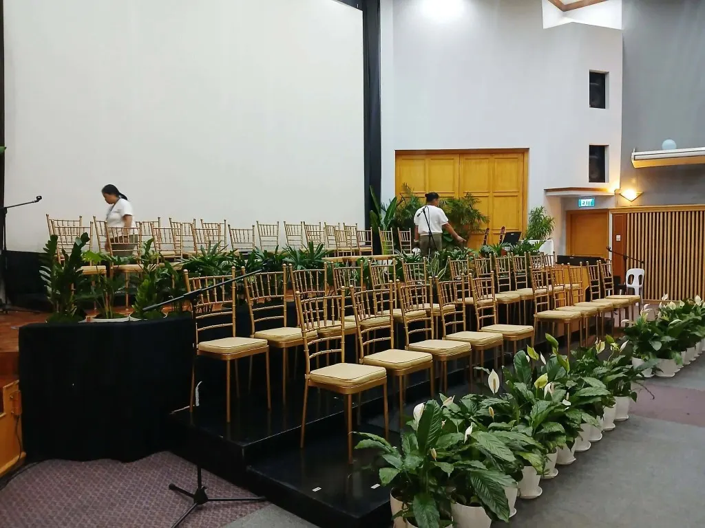 Gold Tiffany chairs arranged on a tiered stage with peace lily plants along the front