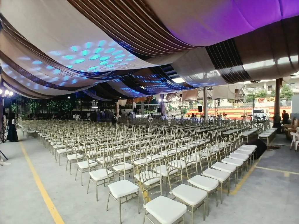 Rows of gold Tiffany chairs under a draped tent ceiling with white and bronze fabric