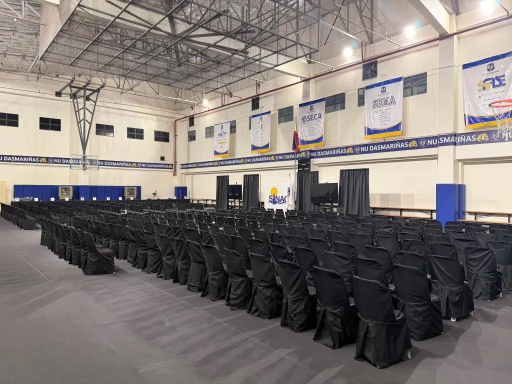 Black-covered chairs filling a gymnasium hall for a school program with stage screens